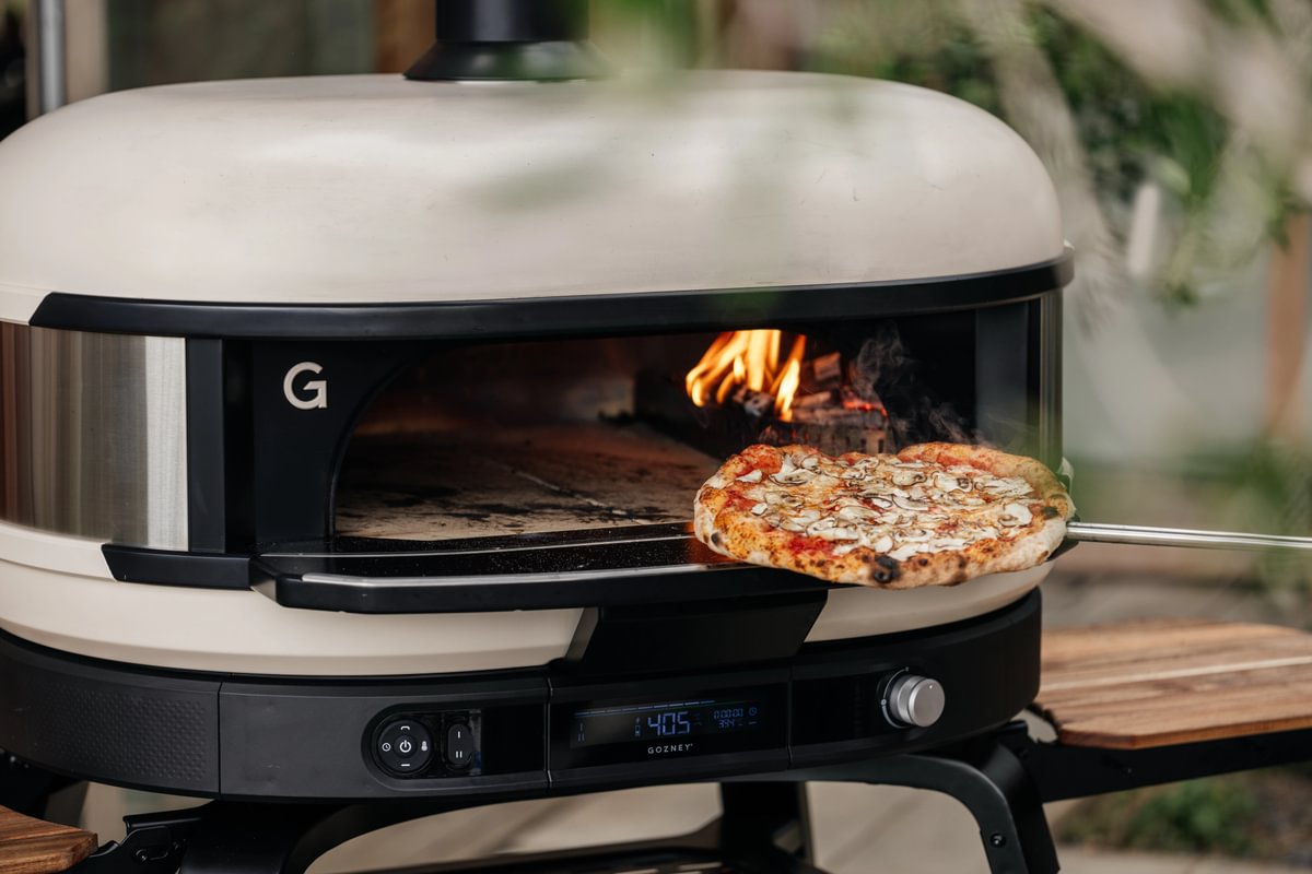 Portable pizza oven with a pizza being cooked outdoors